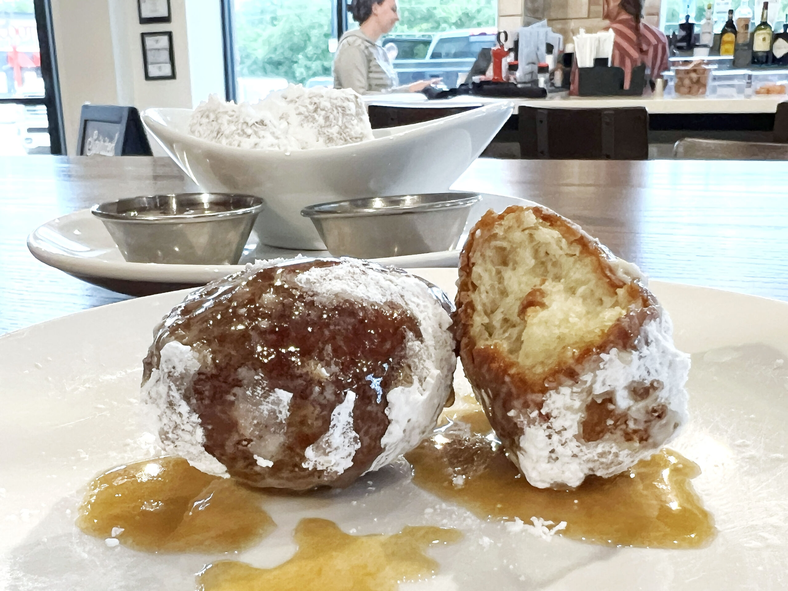 Beignets dripping with rum butter sauce and coated in powder sugar at Broken Egg Cafe Wichita are served as a starter appetizer at brunch.