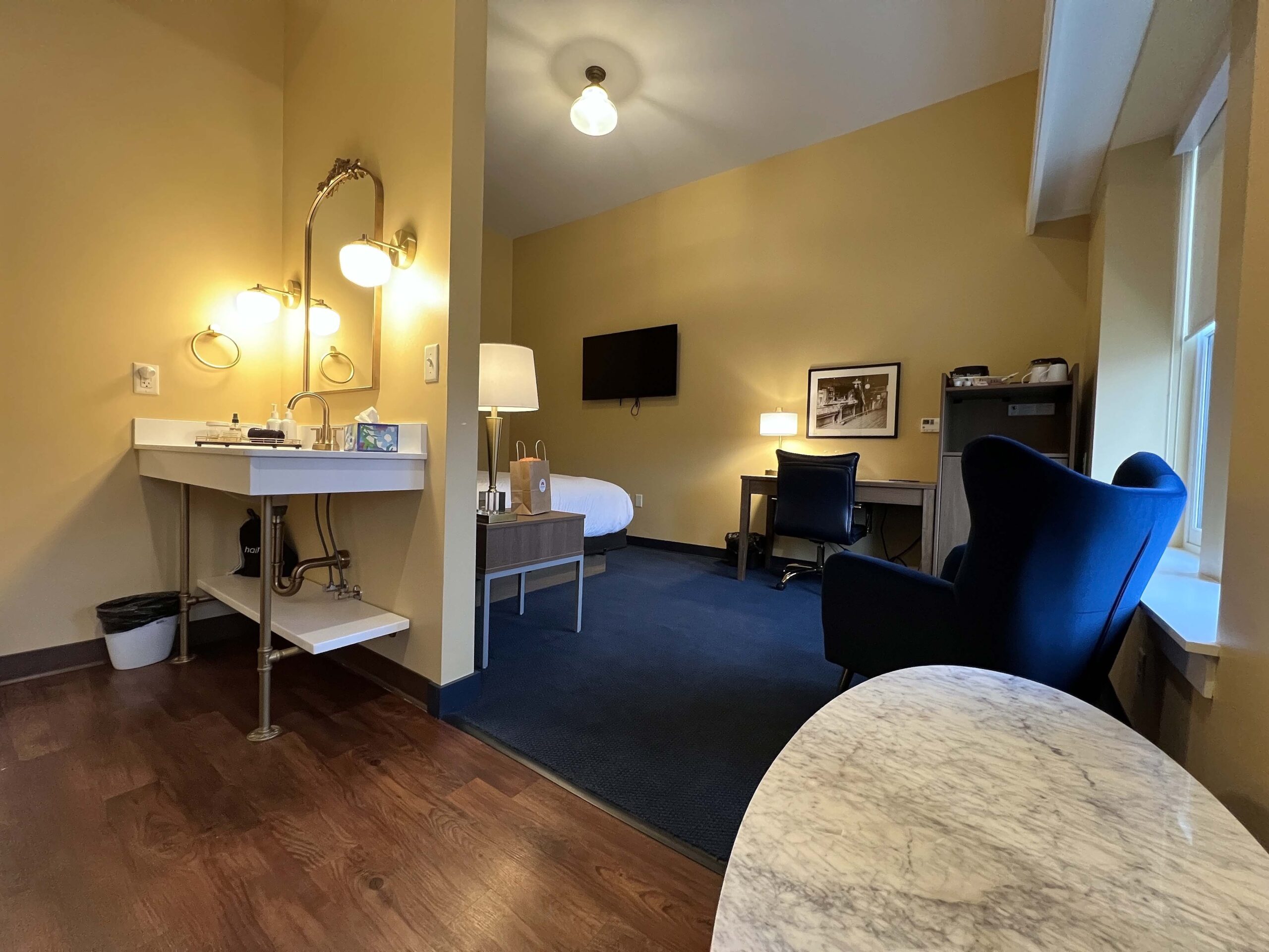 A view of the King room with two windows, bathroom vanity, and lounge chairs near a a desk.