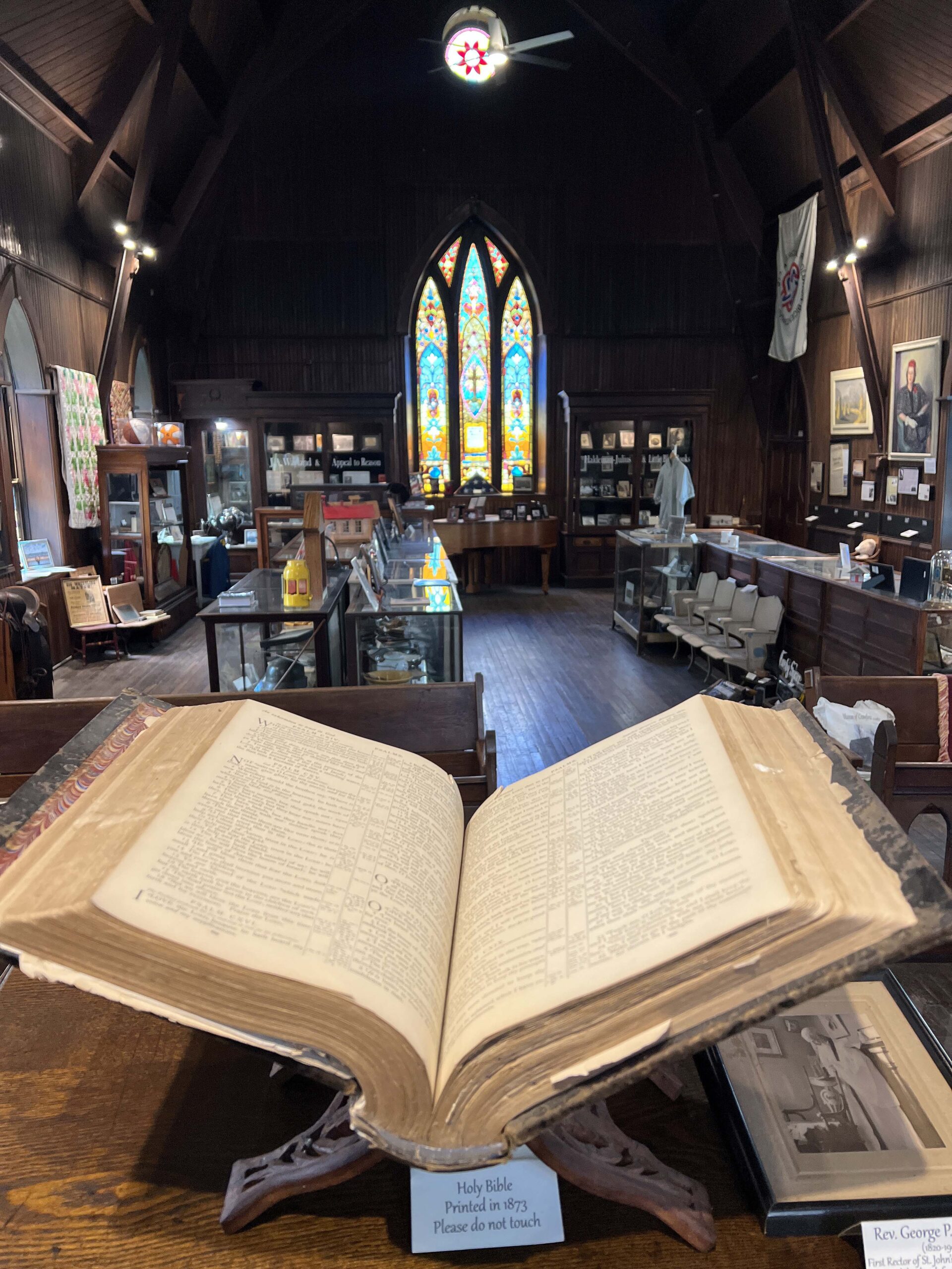 The stained windows at Girard History Museum cascade colorful beams of light onto the church floor on a sunny day.